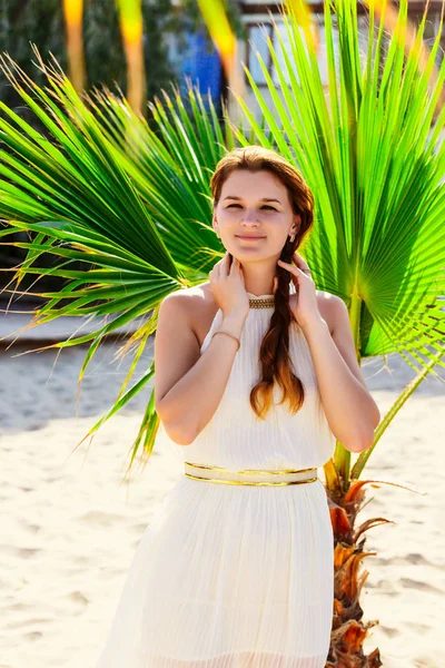 Atraktivní brunetka žena v bílých šatech stojící na pozadí Palmový list — Stock fotografie