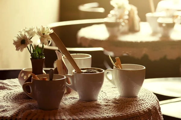 Natura morta. tazze di porcellana bianca e un vaso di fiori si trovano su un tavolo con una tovaglia bianca in una sala da caffè marrone — Foto Stock