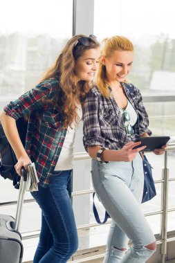 Havaalanında bavul ve tablet vasıl seyir ile iki kız stand. Arkadaş grubu bir gezi