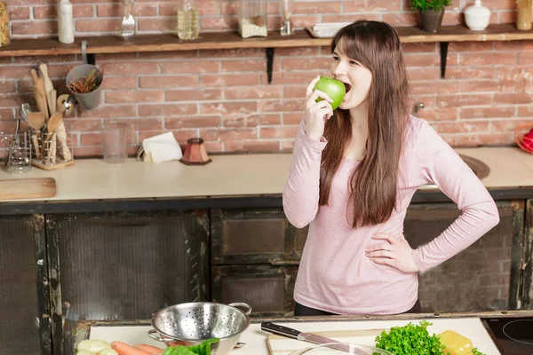 Woman biting a green apple.Young Woman Cooking in the kitchen at home. Healthy Food. Diet.