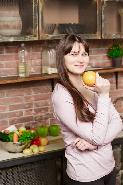 Mujer sostiene una naranja en su mano.Mujer joven Cocinando en la cocina en casa. Comida saludable. Dieta . — Foto de Stock