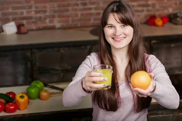 Žena držící skleničku s džusem a oranžovou. Mladá žena vaření v kuchyni doma. Zdravé jídlo — Stock fotografie