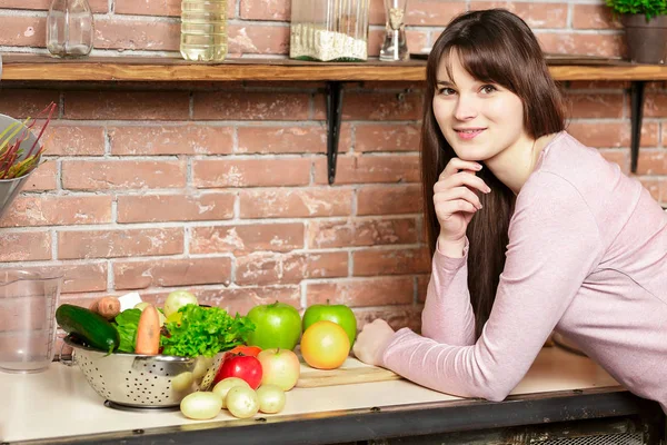 Donna felice cucina in cucina.Donna in cucina si trova vicino a un tavolo con verdure fresche e guarda la fotocamera — Foto Stock