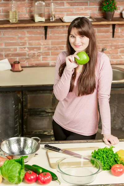 Mujer feliz cocinando en la cocina. mujer está de pie en la cocina cerca de la mesa está sosteniendo una manzana verde — Foto de Stock