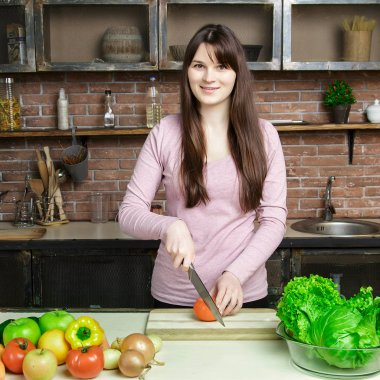 Genç kadın kesme sebze bıçağı kullanarak ve yönetim kurulu pişirme. O mutfakta taze yemek hazırlanıyor.