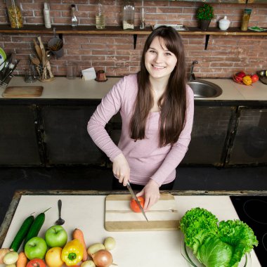 Genç kadın kesme sebze bıçağı kullanarak ve yönetim kurulu pişirme. O mutfakta taze yemek hazırlanıyor.