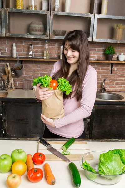 Mujer sosteniendo una bolsa de papel con verduras frescas en la cocina — Foto de Stock