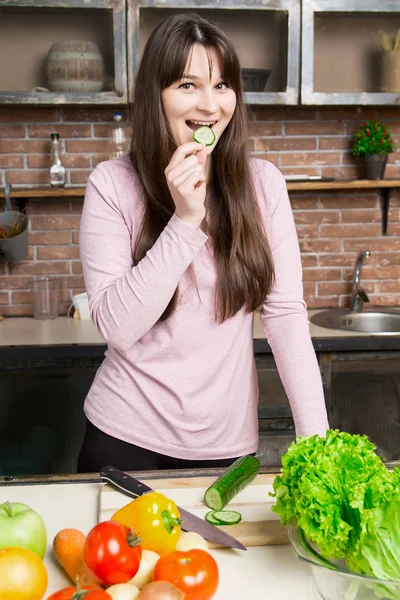 A woman cuts a cucumber in the kitchen with a knife. Preparation of salad and healthy food.