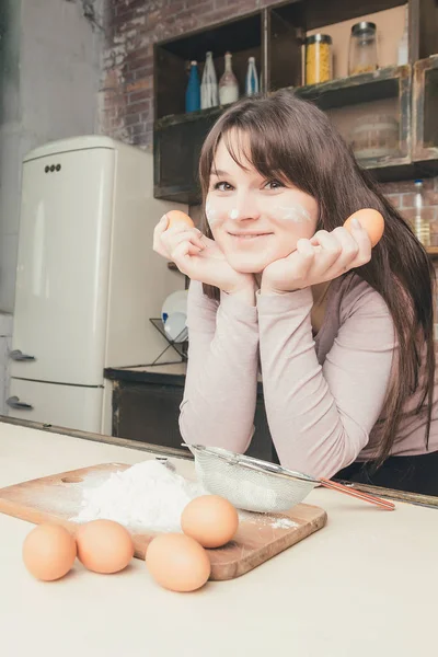 Jovem mulher alegre na cozinha perto da mesa com ovos, farinha . — Fotografia de Stock