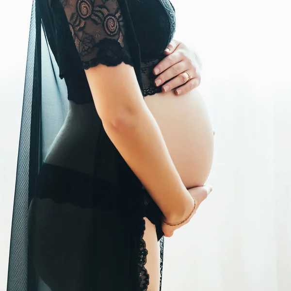 Silhueta de uma fêmea branca grávida em lingerie preta em um fundo branco que segura sua barriga — Fotografia de Stock