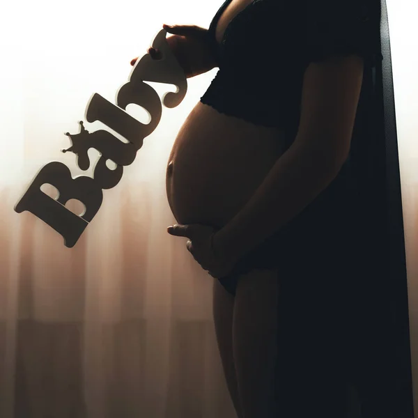 Silhouette of pregnant woman standing in front of window, holding belly.Pregnant woman holding baby letters — Stock Photo, Image