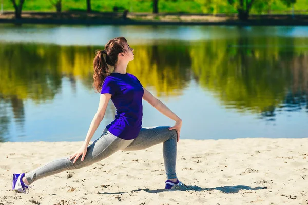 Morena en forma haciendo saltos ponderados en la playa en un día soleado — Foto de Stock