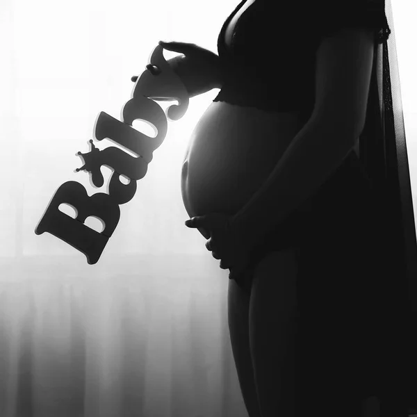 Silhouette of pregnant woman standing in front of window, holding belly.Pregnant woman holding baby letters — Stock Photo, Image