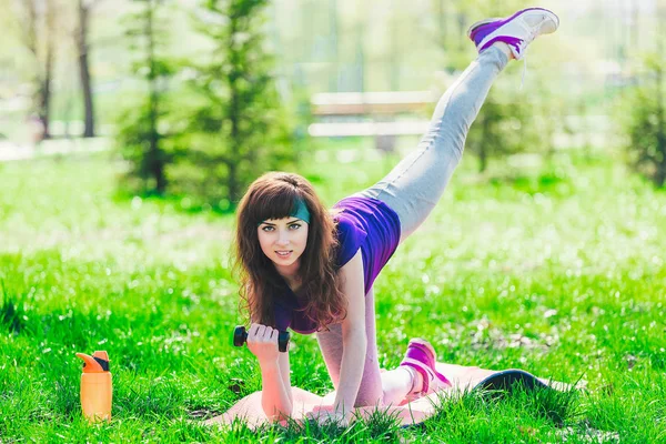 Chica de fitness en el parque y participan en varios ejercicios con mancuerna y estera. morena entra para deportes al aire libre — Foto de Stock