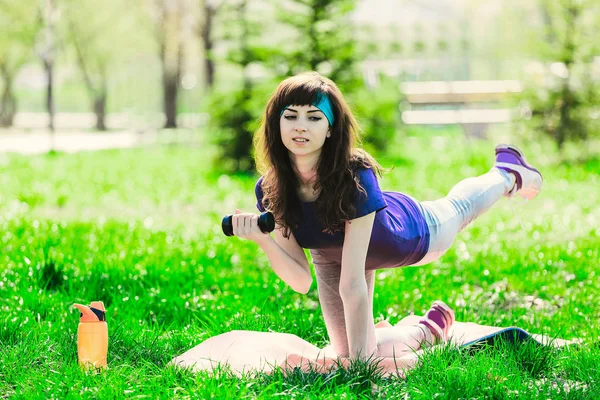 Menina fitness no parque e envolvidos em vários exercícios com haltere e tapete. morena vai para esportes ao ar livre — Fotografia de Stock