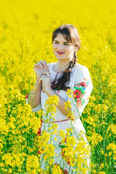 Mulher bonita em ucraniano bordado em pé em um campo de flores de estupro amarelo — Fotografia de Stock