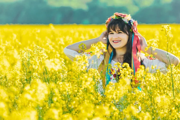 Krásná mladá žena v ukrajinštině vyšívané postavení v oblasti žluté řepky květy — Stock fotografie