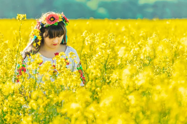 Schöne junge Frau in ukrainischer Bestickung stehend in einem Feld aus gelben Rapsblumen — Stockfoto