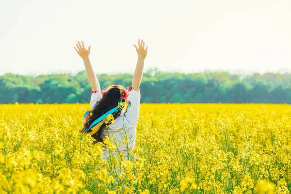 Belle jeune femme en ukrainien brodée debout dans un champ de fleurs de viol jaunes. — Photo