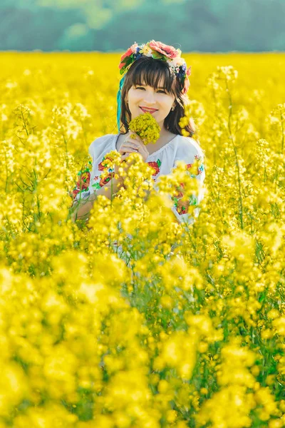 Belle jeune femme en ukrainien brodé debout dans un champ de fleurs de viol jaune — Photo