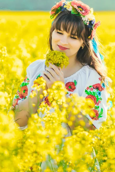 Belle jeune femme en ukrainien brodé debout dans un champ de fleurs de viol jaune — Photo