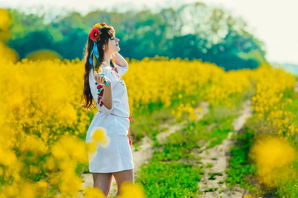 Belle jeune femme en ukrainien brodé debout dans un champ de fleurs de viol jaune — Photo