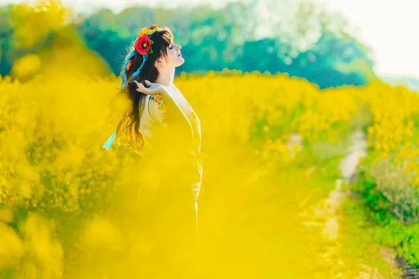 Vacker ung kvinna i ukrainska broderade stående i ett fält av gula våldtäkt blommor — Stockfoto