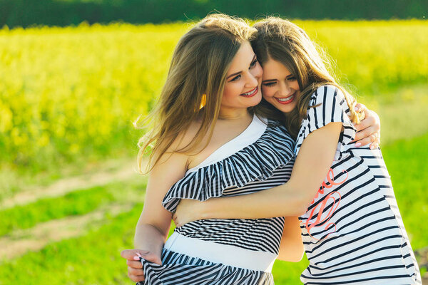 2 beautiful girl in a field of yellow flowers.Mom with daughter or two sisters hugging against the background of a field