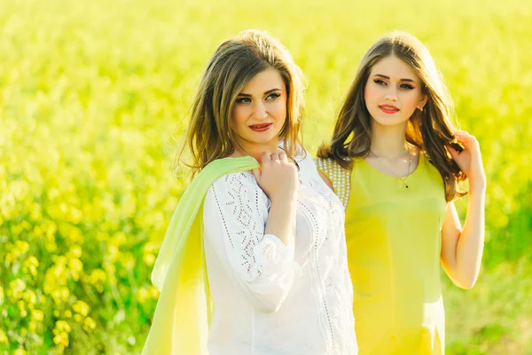 2 hermosa niña en un campo de flores amarillas.Mamá con hija o dos hermanas abrazándose contra el fondo de un campo —  Fotos de Stock