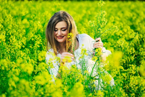 Jeune femme en robe blanche recueille dans le champ des fleurs jaunes . — Photo