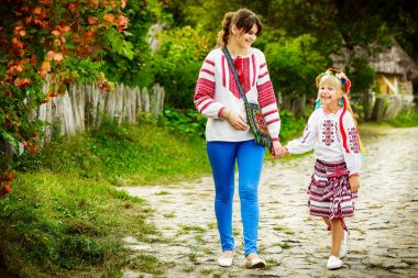 Anne ve kızı halk kostümleri yolda yürüyor. Kadın ve küçük kızı el ele tutuşarak etrafında yürüyor