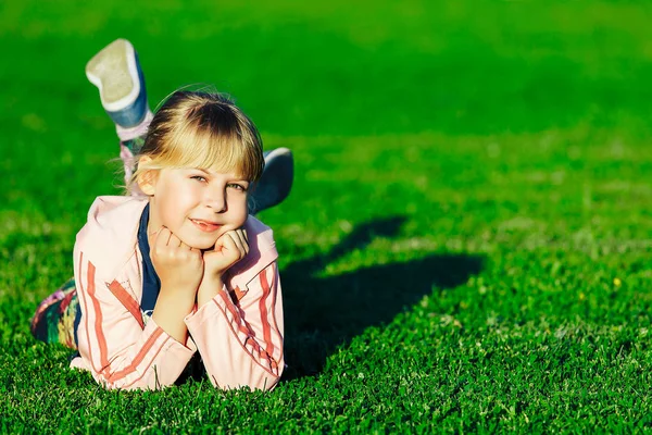 Маленька дівчинка з світлим волоссям лежить під відкритим небом на зеленій траві і дивиться на камеру . — стокове фото