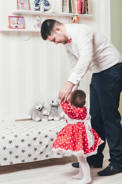 Der Vater hält eine einjährige Tochter an der Hand und hilft ihr beim Gehen. Papa und kleine Tochter spielen im Zimmer — Stockfoto