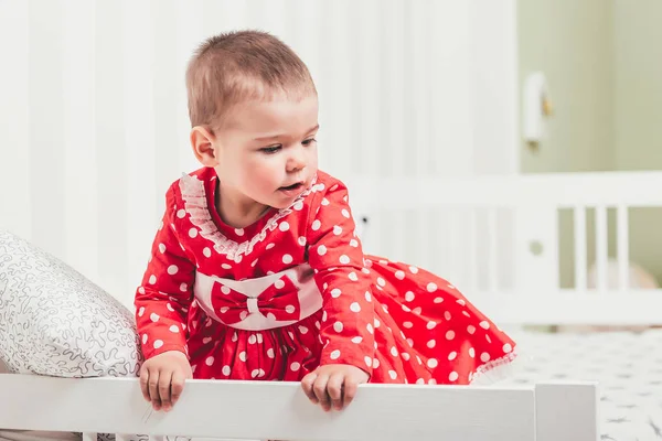 Ein einjähriges Mädchen in einem roten Kleid sitzt auf einem Bett in einem Zimmer — Stockfoto