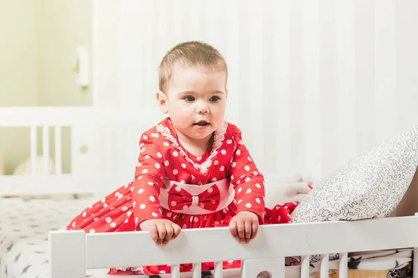 Ein einjähriges Mädchen in einem roten Kleid sitzt auf einem Bett in einem Zimmer — Stockfoto