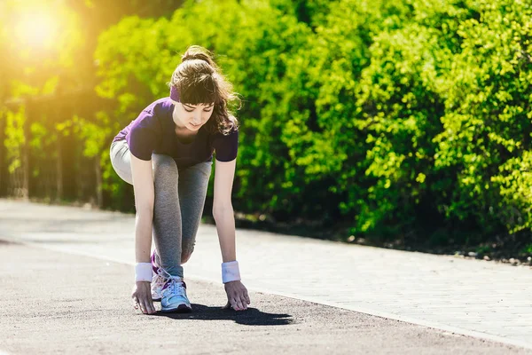 La mujer comienza a correr. Una joven en ropa deportiva se prepara para correr en la naturaleza después de tomar un comienzo bajo — Foto de Stock