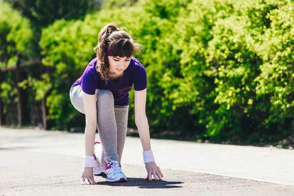 La mujer comienza a correr. Una joven en ropa deportiva se prepara para correr en la naturaleza después de tomar un comienzo bajo — Foto de Stock