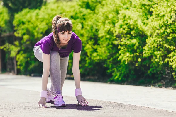 La donna inizia a correre.Una giovane ragazza in abbigliamento sportivo si prepara a correre sulla natura dopo aver preso una partenza bassa. — Foto Stock