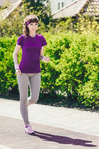 Chica en una camiseta azul corre sobre el fondo de matorrales verdes. El concepto de deporte y estilo de vida saludable . — Foto de Stock