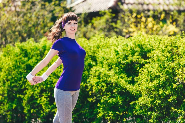 Chica en una camiseta azul está haciendo deportes en la naturaleza contra el telón de fondo de bushes.young mujer corriendo en el parque — Foto de Stock