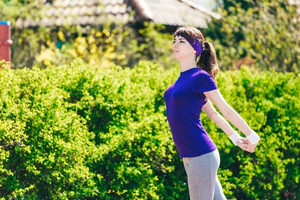 Girl in a blue T-shirt is doing sports in nature against the backdrop of bushes.young woman jogging in the park — Stock Photo, Image