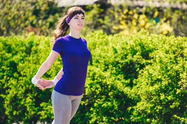 Ragazza in una t-shirt blu sta facendo sport in natura sullo sfondo di bushes.young donna jogging nel parco — Foto Stock