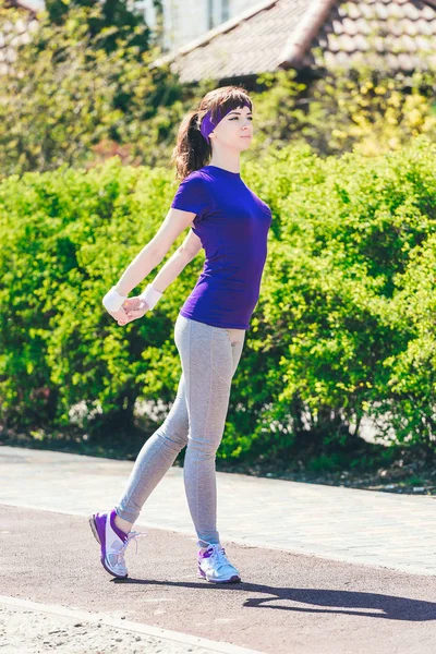 Chica en una camiseta azul está haciendo deportes en la naturaleza contra el telón de fondo de bushes.young mujer corriendo en el parque — Foto de Stock
