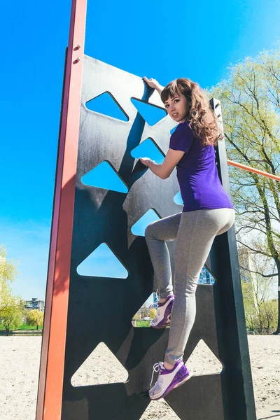 Sports equipment in the park. Rope and climbing ladder.Young woman on a climbing ladder — Stock Photo, Image