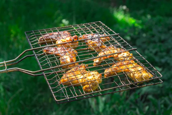 On a grill grate fried chicken pieces on a background of washed greens — Stock Photo, Image