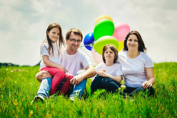 Glückliche Familie sitzt mit Luftballons im Freien an einem warmen Sommertag. — Stockfoto