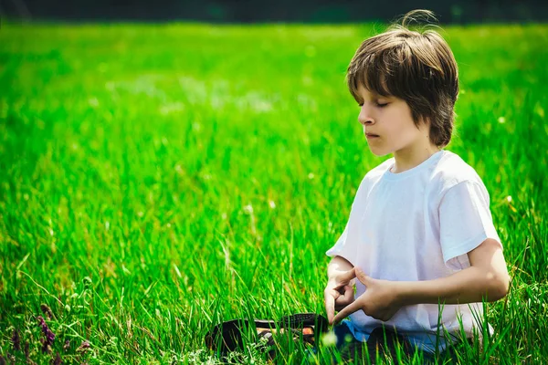 Gözlerini kapatma meditasyon poz, kollarını ve bacaklarını ile yeşil çimenlerin üzerinde tişört oturur bir beyaz bir çocuk geçti.