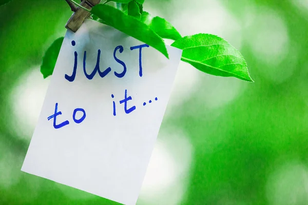 Motivating phrase just to it. On a green background on a branch is a white paper with a motivating phrase. — Stock Photo, Image