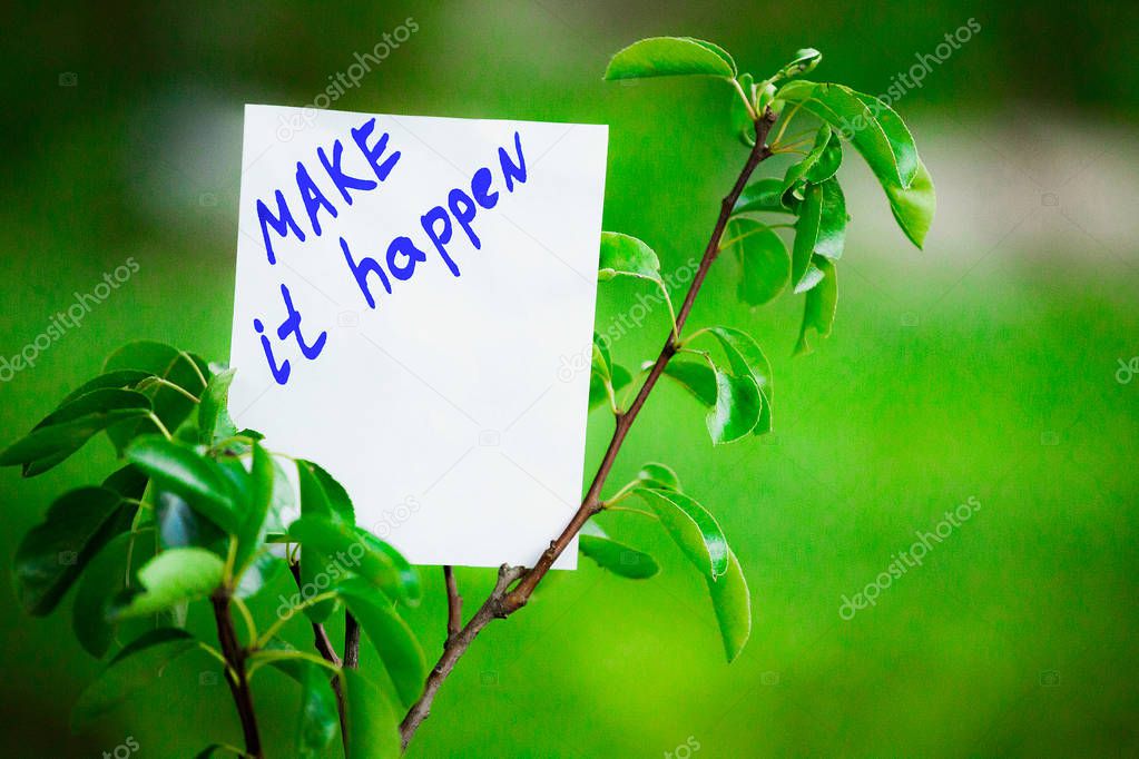 Motivating phrase make it happen. On a green background on a branch is a white paper with a motivating phrase.