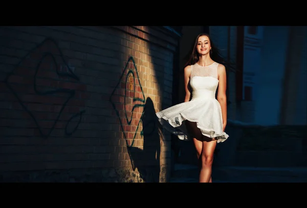 Молода жінка в короткій білій сукні йде по покинутій вулиці на фоні стіни — стокове фото